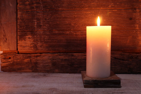 the burning luxury aromatic scented pillar candle glass are on the wooden table with background of the vintage wooden wall of the cottage in the living room during christmas party celebrationの写真素材