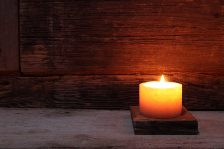 the burning luxury aromatic scented pillar candle glass are on the wooden table with background of the vintage wooden wall of the cottage in the living room during christmas party celebrationの写真素材