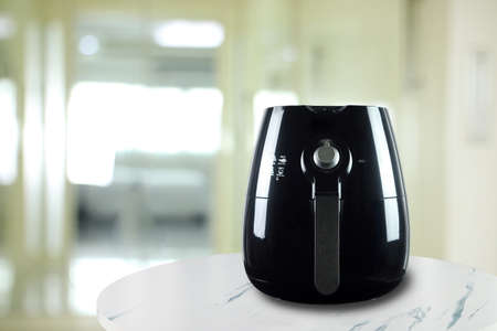 the black air fryer or oil free fryer appliance is on the white marble table with background of the nice kitchen in the morningの写真素材