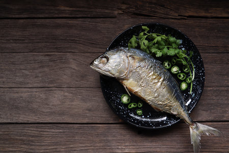 fried mackerel fish with chilli and coriander in the black dish is served on the wooden table in traditiional Thai restaurant for lunchの写真素材