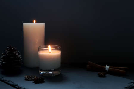 the burning luxury aromatic scented candle glass on the black table with spices on background of...