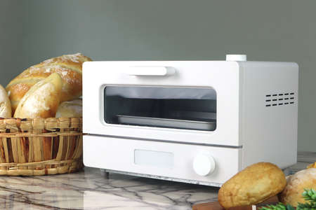 white modern design toaster oven is on the table with homemade toast breads on grey cement wall background in the kitchen room during chritmas partyの写真素材