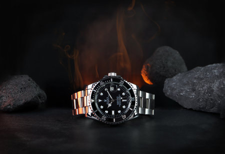 The Rolex vintage wristwatch ceramic bezel model black oyster perpetual submariner date 39 mm display on black table with background of flame and rocks in the dark shelf of luxury watch exhibitionのeditorial素材