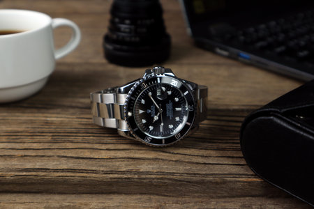 luxurious Rolex vintage wristwatch ceramic bezel model black oyster perpetual submariner date 40 mm is put on the wooden table with a notebook and a cup of coffee in the morning while working timeのeditorial素材