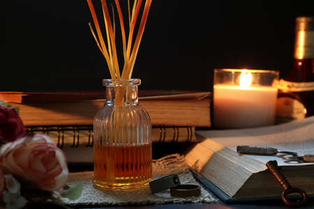 aroma scented reed diffuser bottle or air freshener is on wooden table with a few books , old keys , rings and rose flowers in the living room of the house to creat relax ambient for reading bookの写真素材
