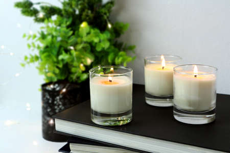 luxury lighting aromatic scented glass candles and a few books are on white table to creat romantic and relax ambient in the white bedroom with background of small plant and led light on valentine dayの写真素材