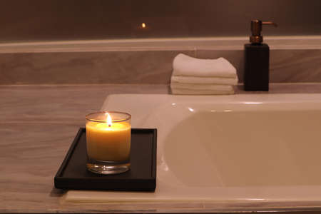 aromatic scented candle glass is put on the white marble bathtub in a luxury white bathroom toilet to creat relax and cozy and clean ambientの写真素材