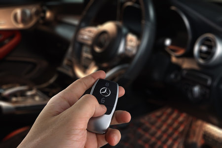 left hand holding car remote key of Benz c200 coupe AMG dynamic model with background of car steering wheel and led speedmeter speed gauge with navigator idrive display inside cabiのeditorial素材