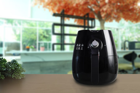 a black deep fryer or oil free fryer , air fryer appliance is on brown wooden table in nice interior design kitchen dinning room of the house during cooking dinner for family membeの写真素材