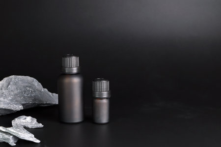 black bottle of natural organic essential oil and massage oil are on the black table with some of rocks and background of black cement wall in the houseの写真素材