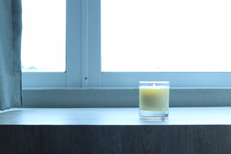 the burning luxury aromatic scented candle glass decorated on the wooden table to make better ambient scent on valentine day with background of sunlight from the window in morningの写真素材