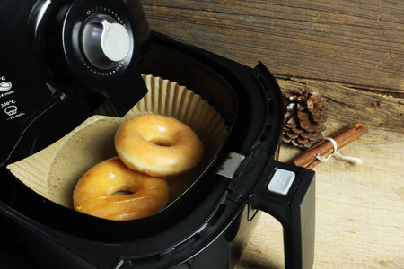 homemade organic wheat grain doughnut or donut are baked by using a black air fryer or oil free fryer appliance for being food in the Christmas party with background of old woodenの写真素材