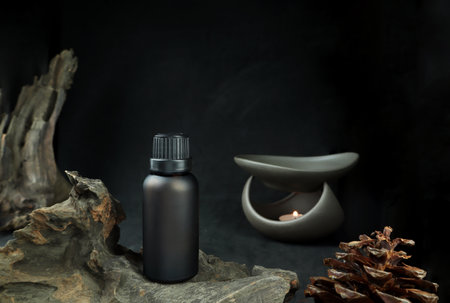 fragrance or essential oil bottle is on wooden table with pine cone , small log and background of nice ceramic aroma oil burner with tealight candle on black cement wall in livingの写真素材