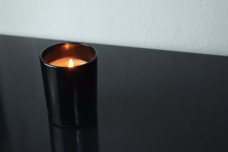 luxury aromatic scented candle glass is on black glass table with a few rocks and background of white stone wall in bedroom to create relax winter cozy ambient on Christmas partyの写真素材