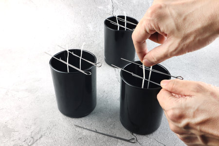 metal wick centering tool for making candle is used to set cotton wick on black glass on stone table...