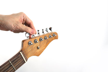 Close-up of a hand adjusting guitar tuning pegs on the headstock, showing guitar tuning process and...