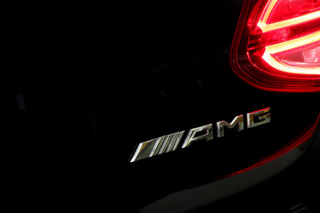 AMG logo at rear trunk of Mercedes Benz luxury car, illuminated by red taillight at night. close up...