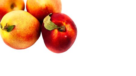 four ripe yellow and red nectarines with green leaves isolated on a white backgroundの写真素材