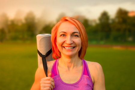 Beautiful woman smiling with a yoga mat on the background of the park.の写真素材