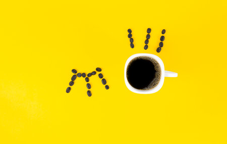 Morning drink concept. Coffee beans and a cup of coffee form closed and open eyes on a yellow background , indicating waking up after a cup of coffee.の写真素材