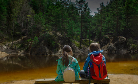 little boy and a little girl are sitting on a bench near a mountain lake.の写真素材
