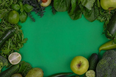 Variety of green fruits and vegetables displayed neatly on green background.の写真素材