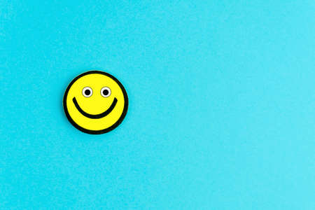 Yellow emoticon with funny eyes on bright blue background. Good day wishes. Copy space for your textの写真素材