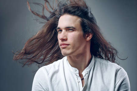 Long haired handsome man. Portrait of guy in motion. Isolated sexy boy in white shirt in studioの写真素材