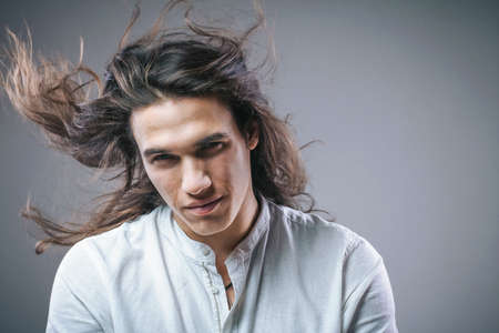 Long haired handsome man. Portrait of guy in motion. Isolated sexy boy in white shirt in studioの写真素材