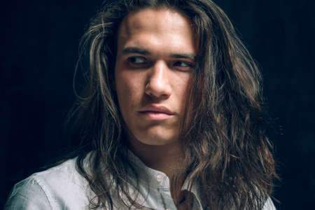 Handsome calm man. Portrait of a young muscular guy with long hair. Strong boy on an isolated dark background in the studioの写真素材