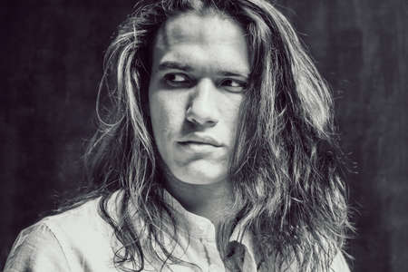 Handsome calm man. Portrait of a young muscular guy with long hair. Strong boy on an isolated dark...