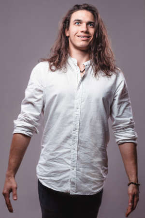 Funny guy with surprised expression. Comic cheerful young man with long hair on isolated background in studioの写真素材