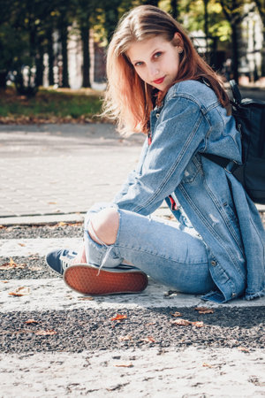 Sitting girl in denim suit in casual street style. Teenager in bright sun outdoorsの写真素材