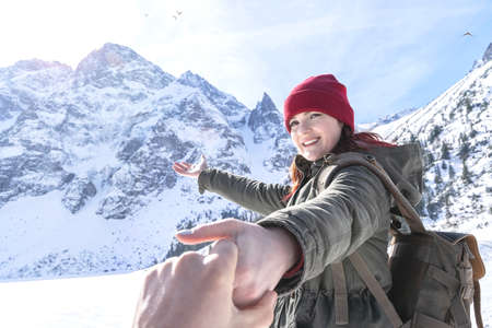 Follow me. Happy smiling girl with backpack in snowy mountains invites you travel. Couple with active lifestyle. Adventure. Tourism conceptの写真素材