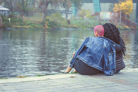 Love between same-sex couple. Sitting lesbian and hug outdoors. Back viewの写真素材