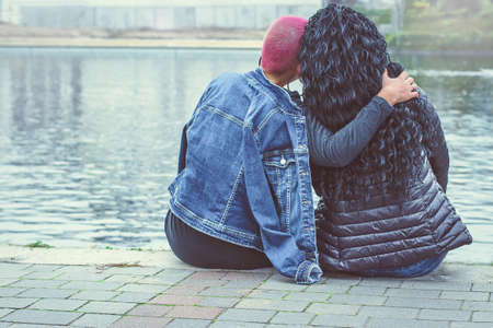 Love between same-sex couple. Sitting lesbian and hug outdoors. Back view