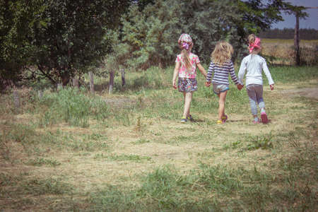 Three little girls walking outdoors holding hands. Girlfriends or sisters. Childhood. Friendship. Kids playing outside summerの写真素材