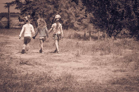 Three little girls walking outdoors holding hands. Girlfriends or sisters. Childhood. Friendship. Kids playing outside summer. Black and white photo. Vintage. Retroの写真素材