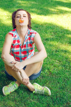 Carefree girl blowing chewing gum outdoors in red checkered shirt. Naughty charismatic teenager in casual style on background of green grassの写真素材