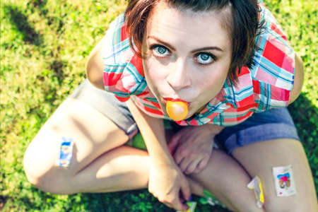 Carefree girl blowing chewing gum outdoors in red checkered shirt. Naughty charismatic teenager in casual style on background of green grassの写真素材