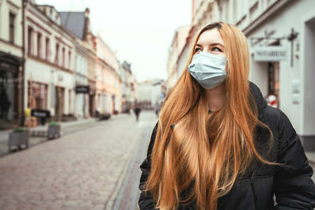 Portrait of girl in protective mask on city street. Beautiful young woman with long hair outdoors. Health careの写真素材