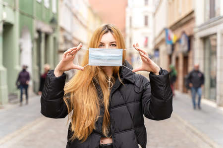 Portrait of girl in protective mask on city street. Beautiful young woman with long hair outdoors. Health careの写真素材