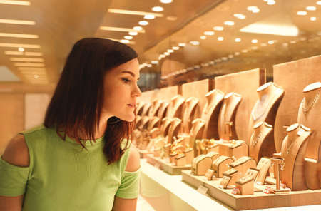 Pretty woman looking at jewelry in store window. Customer near jewelery. Dreamy sexy girl chooses silver, gold, diamonds, precious stones. Purchaserの写真素材