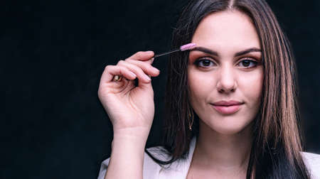 Brunette shows eyebrow tweezers in hands. Girl beautician with tool in hands on white background in studioの写真素材