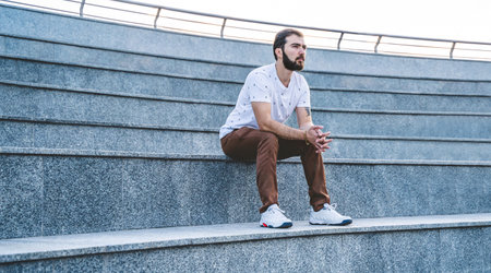 Stylish guy near brick wall drinks coffee. Hipster man with beard on city streetの写真素材