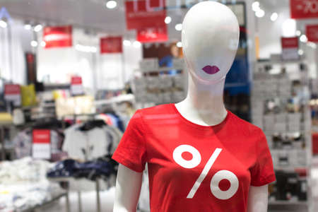Female mannequin in a red T-shirt with the word percent. White mannequin with red lips. Clothing advertising and sale, sales, seasonal discounts, black friday. Fashion businessの写真素材