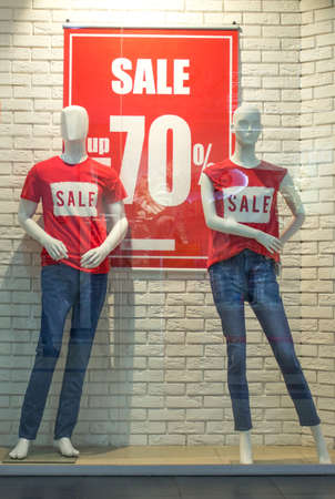 wo female mannequins in red T-shirts and blue jeans in a shop window against a white brick wall background. Promotional 70 percent discount. Black friday cheap clothesの写真素材