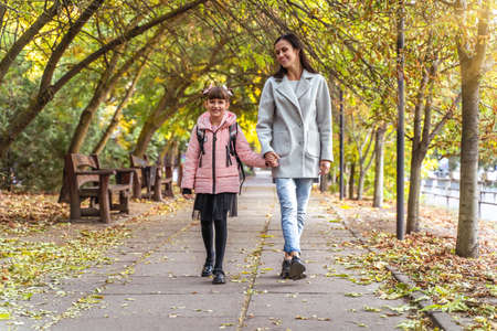 UKRAINE, KHERSON - October 4, 2021: Mom and daughter hold hands outdoors. Happy girl goes to school. Everyday lifeの写真素材