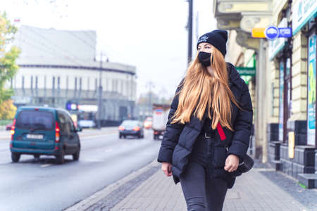 POLAND, BYDGOSZCZ - 12 november 2020: Girl student in protective mask walks down street near traffic. Young woman in casual style. Citizenのeditorial素材