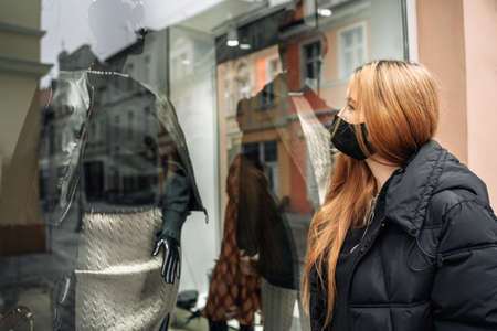 Woman looks at mannequin in shop window. Girl customer near store. Black Friday. Female shoppingの写真素材